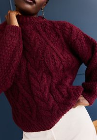 Bordowy sweter dziergany z wzorem warkocza, z wysokim kołnierzem i prążkowanym dołem; fakturowana wełna zwiększa ciepło i atrakcyjność wizualną.