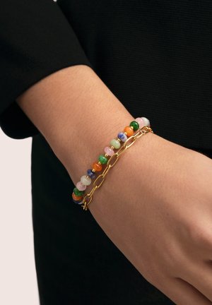 Handgelenk mit zwei Armbändern: eines mit mehrfarbigen runden Perlen, das andere eine goldene Kette mit länglichen Gliedern.