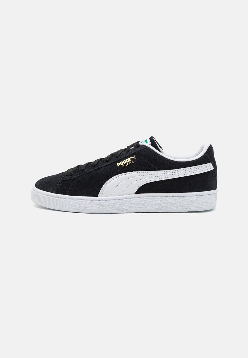 Black suede sneakers with white accents, featuring a textured rubber sole, flat black laces, and gold logo detail on the side.