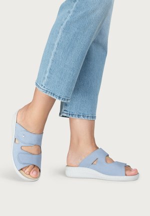Light blue open-toe slip-on sandals with cut-out details worn with cropped light blue jeans on a neutral background.