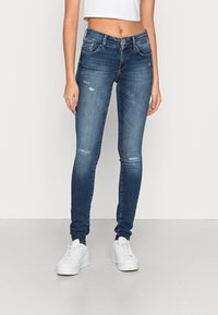 Jeans de mezclilla ajustados en azul medio con acentos desgastados, con una cintura de altura media, cierre de botón de metal y cinco bolsillos.
