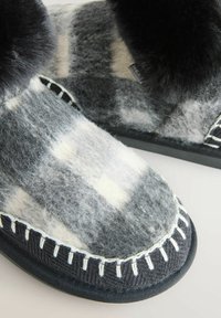 Wool felt slippers in gray and white with black fur cuff, featuring decorative stitching and a durable black fabric sole.