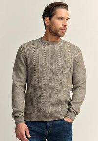 Light gray knitted sweater featuring a textured pattern with vertical cables, round neck, and ribbed cuffs and hem, worn with dark blue jeans.