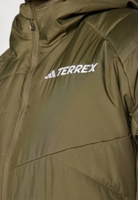 Oliven grøn isoleret jakke med lynlåslukning, udstyret med hætte og hvid "TERREX" logo. Materialet har en let glans og blød tekstur.