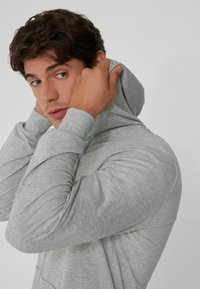Grauer Hoodie mit langen Ärmeln, weicher Textur und lässigem Schnitt. Zeigt Details des Stoffes und der Nahtlinien.