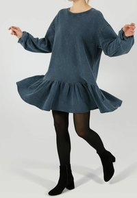 Modrý oversized svetr šaty se volánkovým lemem, dlouhými rukávy a kulatým výstřihem, zkombinované s černými kotníkovými botami a punčochami.