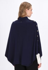 Poncho tricotat �înnuștrit cu colier înalt, tiv rotund și accente de butoane aurii pe laterale. Textură netedă și croi lejer.