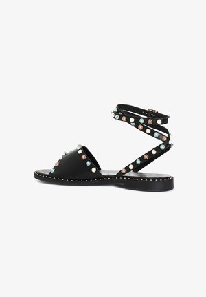 Sandal in pelle nera con punta aperta, fascetta incrociata alla caviglia e borchie decorative colorate. Suola piatta con dettaglio di cuciture a contrasto.