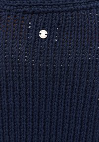 Marinblå stickad tyg med en strukturerad, öppen mönstring och en liten, rund silverdetalj märkta "Mustang."