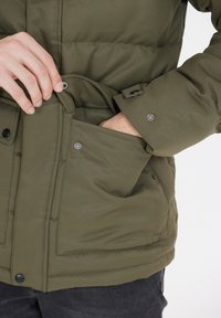 Olivengrøn pufferjakke med lynlås-lomme og trykknaplukninger, med en glat tekstur og polstret design til varme.