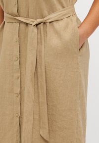 Beigefarbenes Leinenkleid in Knielänge mit durchgehender Knopfleiste, einem abnehmbaren Gürtel und Taschen auf jeder Seite. Strukturierter, leichter Stoff.