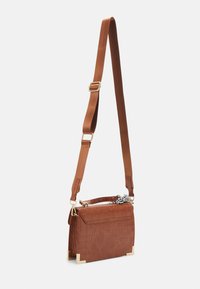 Hnědá crossbody kabelka z kůže s krokodýlím vzorem, nastavitelným popruhem, zlatými ozdobami na rozích a malým černo-bílým textilním detailem na rukojeti.