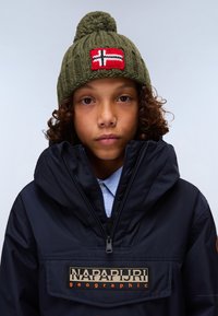 Gorrón de punto verde oliva con pompón y parche de la bandera noruega roja; chaqueta impermeable azul marino con bolsillo con cremallera y logo de la marca.