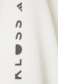 Hvid atletisk stof med en struktureret overflade. Har sort tekst og en trekantet sort detalje i øverste venstre hjørne.