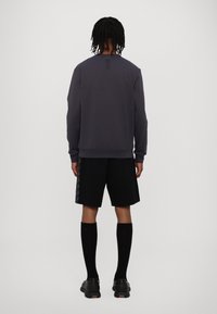 Felpa grigia scura con maniche lunghe, polsini a coste e collo a giro. Abbinata a pantaloni corti neri con dettagli laterali, calze nere fino al ginocchio e scarpe.