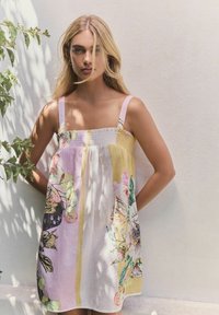 Kukallinen mekko, jossa on smockattu yläosa, neliökaula-aukko ja ohuet olkaimet. Värit sisältävät keltaista, vaaleanpunaista ja valkoista, joissa on kasvitieteellisiä kuvioita.