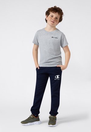 Camiseta gris de manga corta con logo negro, combinada con joggers navy que tienen un logo blanco, y zapatillas verdes con suelas blancas.