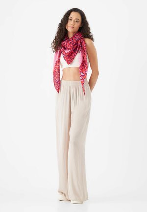 Écharpe à imprimé léopard rose portée autour du cou, associée à un pantalon large beige clair. Tissu lisse et léger avec un design fluide.