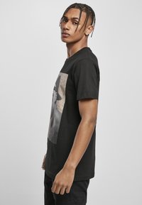 Schwarzes Baumwoll-T-Shirt mit einem großen grafischen Druck auf der Vorderseite. Kurze Ärmel, lockere Passform und glatte Textur.