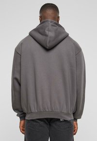 Sudadera gris con capucha ajustable, puños acanalados y cinturilla. Tejido suave con mínima textura, de corte relajado y sin patrones visibles.