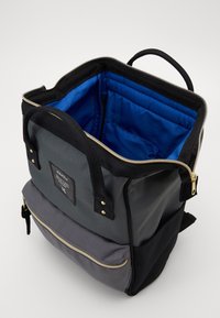 Szara i czarna plecak z niebieskim wnętrzem, otwarty zamek błyskawiczny na górze, przednia kieszeń na zamek błyskawiczny oraz czarne uchwyty na białym tle.