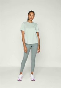 T-shirt atletico verde chiaro a maniche corte abbinato a leggings grigi aderenti. Le scarpe sono bianche con dettagli viola.
