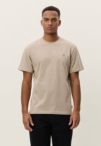 Beige bomulls-T-skjorte med korte ermer og rund hals, med en liten blå "II"-logo på brystet. Enkelt design og vanlig passform.