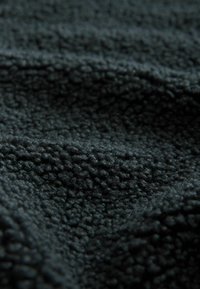 Tessuto grigio scuro testurizzato con una superficie morbida e pelosa, caratterizzato da pattern in rilievo e una qualità tattilmente piacevole, adatto a varie applicazioni.