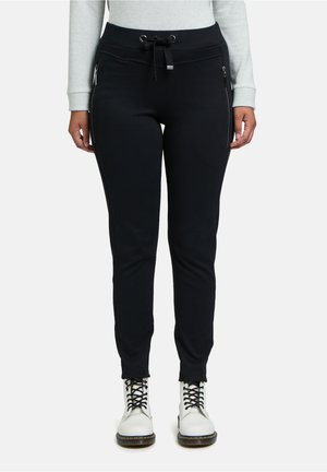 Black sweatpants with a drawstring waist, side zip pockets, and a tapered leg design. Soft fabric texture, paired with white lace-up boots.
