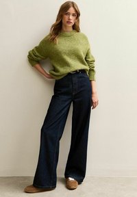 Maglione verde lavorato a maglia con collo rotondo, abbinato a jeans a gamba larga blu scuro a vita alta. Scarpe casual marroni completano l'outfit.