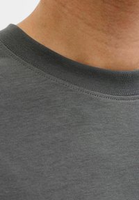 T-shirt en coton gris avec col rond et col côtelé. Le tissu semble lisse avec une texture subtile et des détails de couture.