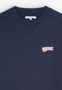 Felpa blu navy, tessuto testurizzato, colletto a girocollo, con un piccolo logo "SCALPERS" rosa e bianco sul petto.