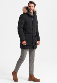 Schwarze Puffy-Jacke mit einem mit Fell gefütterten Kapuzenkragen, zwei Fronttaschen und einem Reißverschluss. Tragend mit grauen Cargo-Hosen und braunen Ankle Boots.