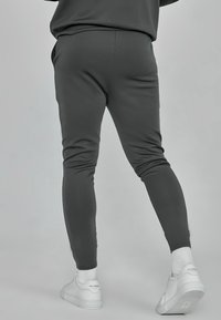 Pantaloni joggers grigio scuro a sigaretta realizzati in tessuto morbido, con tasche laterali e polsini a costine, abbinati a sneakers bianche e calze texturizzate.