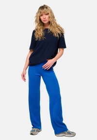 Haut à manches courtes bleu marine associé à un pantalon large bleu vif, tous deux en tissu doux et texturé. Porté avec des baskets grises.