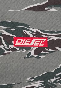 Pezzo di stoffa grigia con un logo Diesel rettangolare rosso, decorato con un motivo mimetico in verde scuro, bianco e nero.