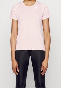 Vaaleanpunainen lyhythihainen urheilupaita pyöreällä kaula-aukolla ja valkoisella Nike-logolla vasemmassa yläkulmassa. Kangas näyttää sileältä ja hengittävältä.