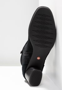 Bottine en daim noir avec bout arrondi, fermeture éclair latérale et semelle en caoutchouc texturée présentant un motif en losange.