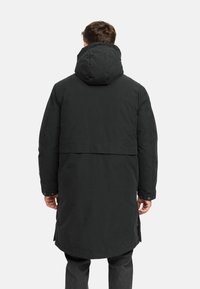 Parka larga negra con capucha, de corte recto y puños abotonados. La parte posterior tiene una costura horizontal a la altura de la cintura para un diseño adicional.