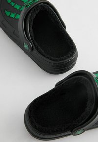 Sabots noirs à enfiler avec un design de toile d'araignée verte, doublure en polaire et côtés perforés pour la ventilation. Semelle en caoutchouc texturée pour une meilleure adhérence.