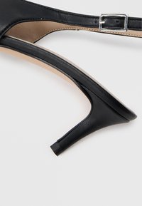 Musta korkokengän malli, jossa on sileä nahkapäällinen, avoimet sivut ja kapea, kapeneva korko. Mukana solkisomiste.