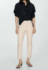 Chemise noire à boutons associée à un pantalon beige clair ajusté et des sandales noires à talons. Tissu lisse avec un design épuré et des poches latérales.