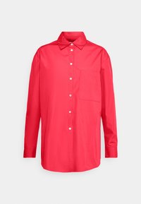 Chemise rouge vif à manches longues avec boutons, col et une seule poche poitrine, présentée sur un fond gris clair.