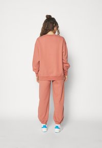 Stofroze sweatshirt en bijpassende joggers van zacht materiaal; losse pasvorm met ribgebreide boorden en enkels; gecombineerd met witte sneakers.