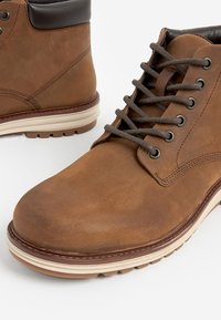 Brune læderankelstøvler med rund tå, mat finish, runde snørebånd, metaløjer og kontrasterende lysefargede gummisåler.