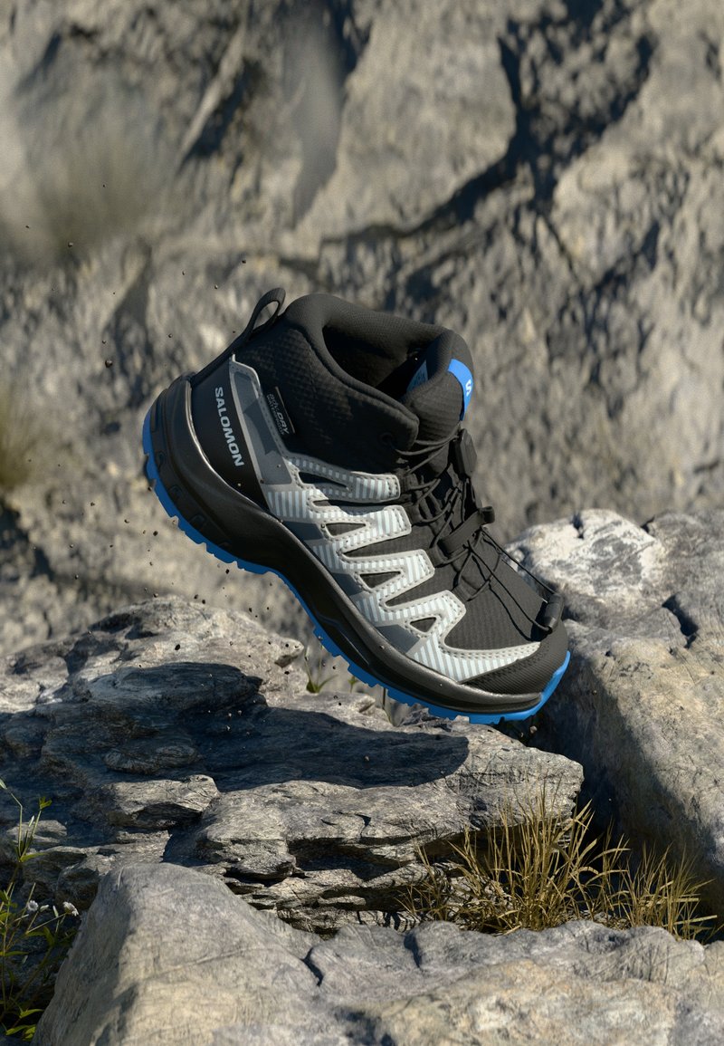 Zapatilla atlética de caña alta en negro y gris con suela de goma, parte superior texturizada y acentos azules. Presenta un diseño de cordones y puntera reforzada.