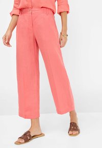 Coral linen wide-leg trousers with front pleats, belt loops, and a button closure. Paired with brown slide sandals.