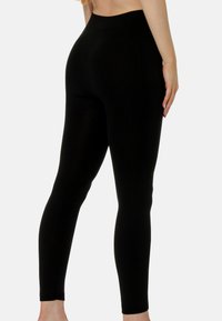 Leggings noirs en tissu lisse et extensible avec une taille haute, ajustés aux jambes, offrant une silhouette épurée.