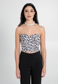 Schwarz-weißer gepunkteter Crop-Top mit Herzausschnitt, der eine taillierte Passform aufweist. Kombiniert mit hochgeschnittenen schwarzen Hosen.