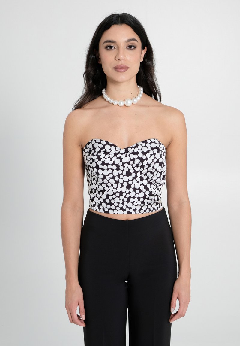 Schwarz-weißer gepunkteter Crop-Top mit Herzausschnitt, der eine taillierte Passform aufweist. Kombiniert mit hochgeschnittenen schwarzen Hosen.